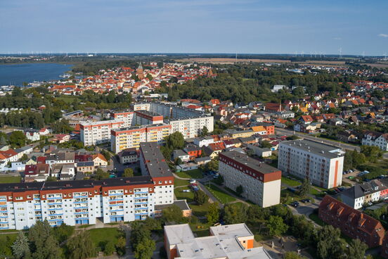 Luftaufnahme von Ribnitz-West mit Wohnblöcken im Vordergrund, Einfamilienhäusern und dem Bodden im Hintergrund.