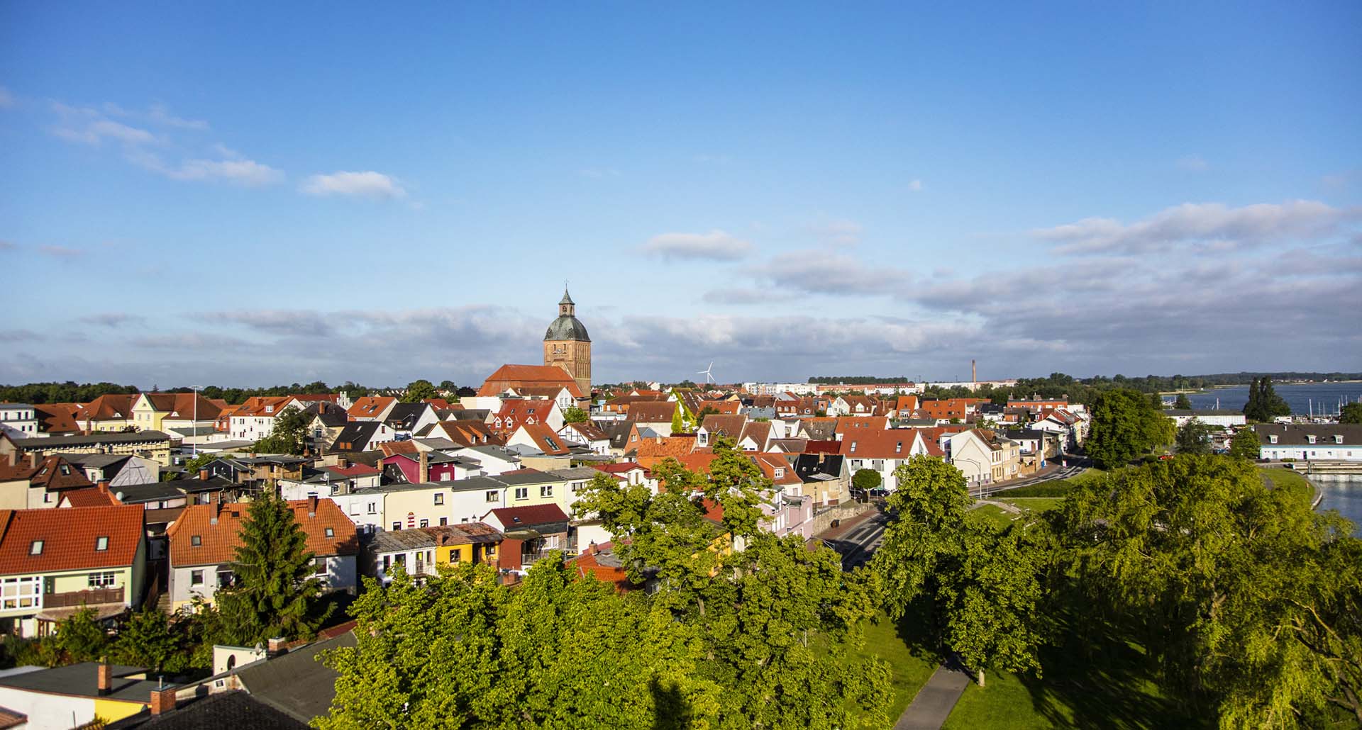 Luftaufnahme der Stadt Ribnitz-Damgarten mit markantem Kirchturm, Wohnhäusern und viel Grün unter blauem Himmel.